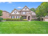 Beautiful brick home featuring manicured lawn, stone accents, mature trees, and a charming front porch at 8070 Clems Branch Rd, Indian Land, SC 29707