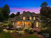 Stunning brick home showcasing a meticulously landscaped front yard, illuminated by warm lighting and a picturesque twilight sky at 266 Riverwood Rd, Mooresville, NC 28117