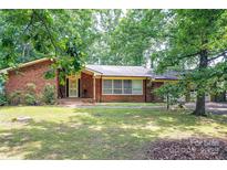 Charming brick home featuring mature trees, an inviting front porch, and lush landscaping for a serene curb appeal at 541 Greenway St, Davidson, NC 28036