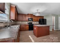 A kitchen features wood cabinets, an island, and black appliances against a light backsplash at 5008 Social Cir, Fort Mill, SC 29707