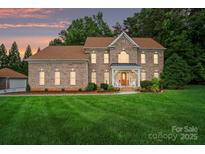 Brick two-story home featuring a manicured lawn and covered front porch with sunset in the background at 6324 Old Fox Hunt Ln, Mint Hill, NC 28227