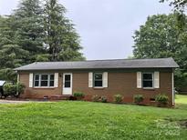 Charming brick home with green trim and shutters surrounded by a lush green lawn and mature trees at 1606 Northwoods Dr, Kings Mountain, NC 28086