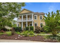 Charming yellow two-story home featuring a welcoming front porch with white columns and beautifully landscaped front yard at 2009 Waterbury Ln, Waxhaw, NC 28173