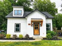 Charming home featuring white vertical siding, a covered wood porch, black trim, and landscaped yard at 125 Todd Nw Dr, Concord, NC 28025