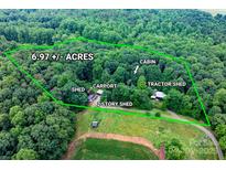 A scenic aerial view of a wooded 6.97-acre lot featuring a cabin, carport, sheds, and a tractor shed at 2951 Evergreen Trl, Vale, NC 28168