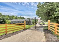 Gated driveway entrance with a wood fence and a decorative metal gate on a sunny day at 117 Autumn Woods Dr, Kings Mountain, NC 28086