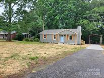 Charming single-story home with a blue door and shutters surrounded by lush greenery and a gravel driveway at 2070 Stirewalt Rd, China Grove, NC 28023