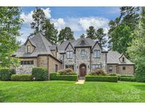 Stunning stone-clad home featuring a manicured lawn and lush, mature landscaping at 3032 Kings Manor Dr, Matthews, NC 28104
