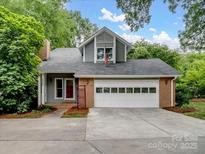 Charming home with a two-car garage and dormer, set amidst lush greenery, features a gray facade and brick accents at 3327 Archdale Dr, Charlotte, NC 28210
