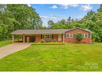 Charming brick home featuring a well-manicured lawn, mature trees, and a convenient covered carport at 44092 Woodhurst Rd, New London, NC 28127