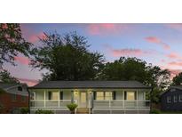 Charming home featuring a welcoming front porch, complemented by the lush, green landscape and a backdrop of the sunset at 4838 Keats Ave, Charlotte, NC 28212