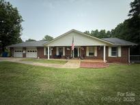 Charming brick home with a covered porch, an American flag, a manicured lawn, and an attached garage at 117 Lincoln Village Dr, Statesville, NC 28677