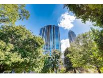 A striking exterior view of a modern high-rise building framed by lush green trees and a clear blue sky at 210 N Church St # 2807, Charlotte, NC 28202