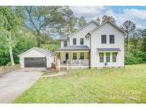 Beautiful two-story farmhouse with white siding, black trim, inviting front porch, and a detached garage at 1062 Willow Ridge Ln, Fort Mill, SC 29707