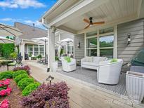 Cozy covered patio area with comfortable white seating, ceiling fan, and adjacent garden beds for relaxing or entertaining at 1226 Restoration Dr, Waxhaw, NC 28173