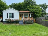 Charming home featuring a covered front porch, yellow door, well-maintained lawn, and lush landscaping at 199 Crowell Sw Dr, Concord, NC 28025