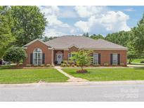 Charming brick home with well-manicured lawn, mature trees, and inviting stone pathway leading to the front door at 502 Roxanne Nw Ct, Concord, NC 28027