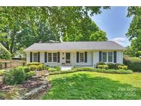 Charming white brick home featuring black shutters, a lush front lawn, and mature trees at 6938 Wrentree Dr, Charlotte, NC 28210