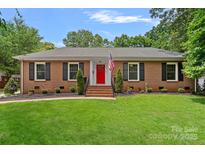 Charming brick ranch with a manicured lawn, red door, and black shutters offers great curb appeal at 6946 Woodstock Dr, Charlotte, NC 28210