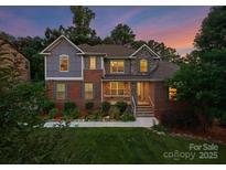 Charming two-story home with brick and stone accents, a manicured lawn, and beautiful landscaping at 7798 Sand Trap Ln, Stanley, NC 28164