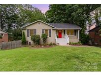 Charming brick home with a red door, green lawn, and flowering plants at 6935 Woodstock Dr, Charlotte, NC 28210