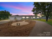 Charming single-story home with manicured front yard and three-car garage, lit by dusk sky at 15020 Ranson Rd, Huntersville, NC 28078