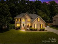 Inviting two-story brick home with manicured lawn, landscape lighting, and mature trees at dusk at 122 Laurel Glen Dr, Mooresville, NC 28115
