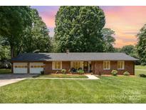 Charming brick home with an attached two-car garage, lush green lawn, and mature trees at 400 S Westover Dr, Monroe, NC 28112