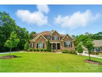 Beautiful two-story brick home featuring a well-manicured lawn and mature trees against a bright blue sky at 463 Langston Place Dr, Fort Mill, SC 29708