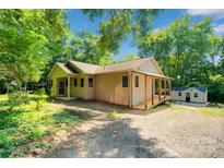 Charming home exterior with covered porch, surrounded by lush greenery, and a storage shed at 3333 Roberta Rd, Concord, NC 28027