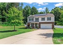 Charming two-story home boasts a well-manicured lawn, long driveway, and a welcoming facade with stone accents and solar panels at 301 Wheat Field Dr, Mount Holly, NC 28120