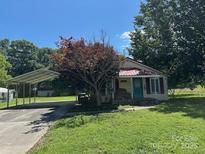 Charming single-story home with a red roof, a large tree, and a metal carport on a sunny day at 1421 N Post Rd, Shelby, NC 28150