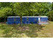A mobile home with a blue exterior and a small porch surrounded by lush greenery and trees at 41042 Dennis Rd, Albemarle, NC 28001