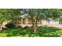 Inviting single-story brick home with a cozy porch and charming curb appeal, surrounded by mature trees and lush landscaping at 116 Woodbark Ln, Kings Mountain, NC 28086