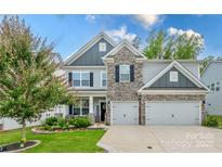 Charming two-story home featuring a stone facade, gray siding, manicured lawn, and a two-car garage at 1054 Thoroughbred Dr, Iron Station, NC 28080