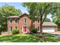 Charming two-story brick home with a manicured lawn, bright red door, and attached two-car garage at 14402 Raynham Dr, Charlotte, NC 28262