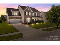 Charming brick two-story home with a manicured lawn and attached two-car garage at twilight at 9937 Violet Cannon Nw Dr, Concord, NC 28027