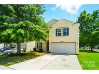 Charming yellow two-story home featuring a two-car garage, blue shutters, a well-manicured lawn, and mature trees at 8604 Rockmoor Ridge Rd, Charlotte, NC 28215