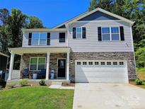 Two-story home featuring stone accents, light gray siding, black shutters, and a two-car garage with blue sky background at 3816 Rosewood Dr, Mount Holly, NC 28120