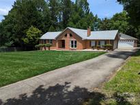 Charming brick home featuring a well-manicured lawn, mature trees, and an expansive driveway at 8007 Caldwell Rd, Harrisburg, NC 28075