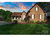 Charming brick home featuring a manicured lawn and mature landscaping, with a picturesque sunset sky at 3831 Riceland Pl, Charlotte, NC 28216