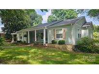 Charming home with light green siding, wooden shutters, and a covered front porch with hanging plants at 415 S Central Ave, Locust, NC 28097