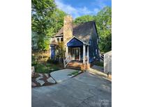 Charming blue two-story home with stone chimney and covered front porch surrounded by lush greenery at 27092 Village Dr, Fort Mill, SC 29708