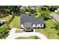 Aerial view of a home with a gray roof, white siding, front porch, gravel driveway, and a fenced in front and side yard at 307 W Sunset Dr, Moore, NC 28110