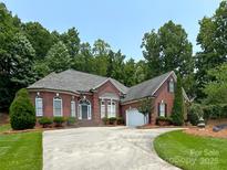 Charming brick home features a well-manicured lawn, a circular driveway, and lush landscaping at 11646 Hidden Forest Ln, Davidson, NC 28036