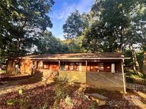 Rustic single-story home with wooden exterior, a full-length porch, and a natural yard shaded by mature trees at 3685 River Rd, Richfield, NC 28137