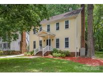 Charming two-story yellow home featuring a welcoming front porch and a lush, landscaped yard with mature trees at 10606 Danesway Ln, Cornelius, NC 28031