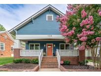 Charming blue home featuring a welcoming porch, brick accents, an orange front door, and a beautiful flowering tree at 1008 Vanizer St, Charlotte, NC 28208