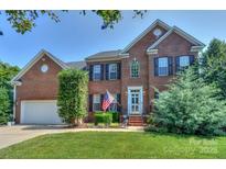 Charming two-story brick home with manicured lawn, American flag, and attached two-car garage at 6873 Lakecrest Ct, Denver, NC 28037