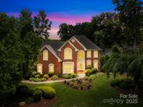 Elegant brick home with manicured lawn, lush landscaping, and warm, inviting exterior lighting at 9514 Hayenridge Ct, Huntersville, NC 28078
